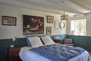 A bedroom with a bed, a nightstand, a desk, a chair, and a window.
