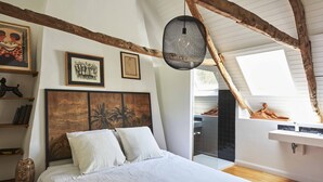 A bedroom with a large bed, wooden beams, a hanging light fixture, and artwork on the walls. - La Maison de L'amiral (Moëlan-sur-Mer)