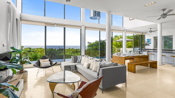 A spacious living area with a large window overlooking a lush landscape, a modern kitchen, and a seating area with a glass coffee table and contemporary furniture. - Stunning contemporary villa with incredible views over the Barbados West Coast (Lower Carlton)