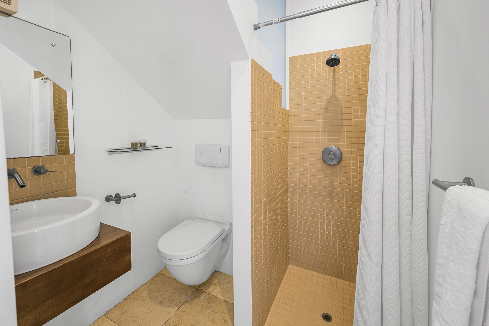 Une salle de bain avec un lavabo blanc, des toilettes et un espace douche aux carreaux de couleur beige.
