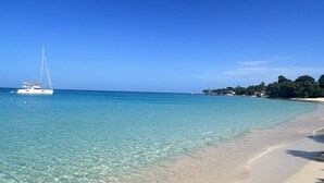 A beach with clear turquoise water, a sailboat, and a distant shoreline with buildings and trees. - Stunning contemporary villa with incredible views over the Barbados West Coast (Lower Carlton)