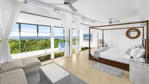A modern bedroom with a four-poster bed, a large window with a view of the ocean, and a ceiling fan. - Stunning contemporary villa with incredible views over the Barbados West Coast (Lower Carlton)
