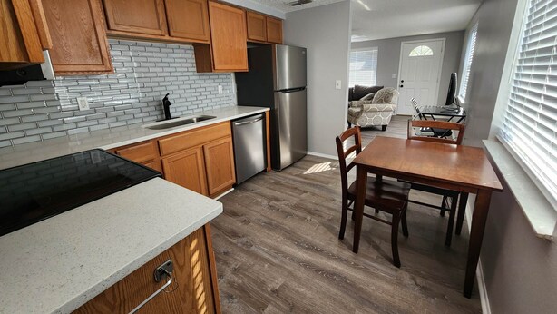 Una cocina moderna con armarios de madera, un refrigerador de acero inoxidable y un comedor con mesa y sillas de madera.