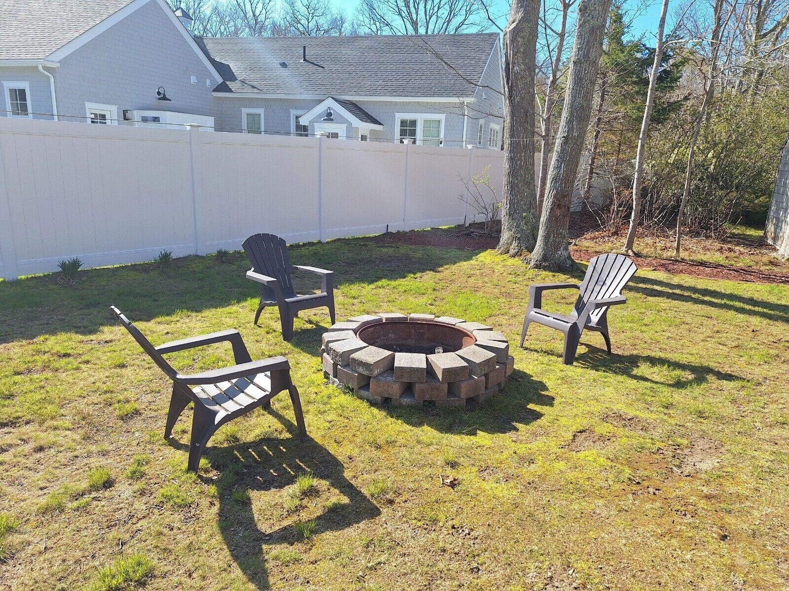 Un jardin avec un foyer, deux fauteuils Adirondack et une clôture blanche.