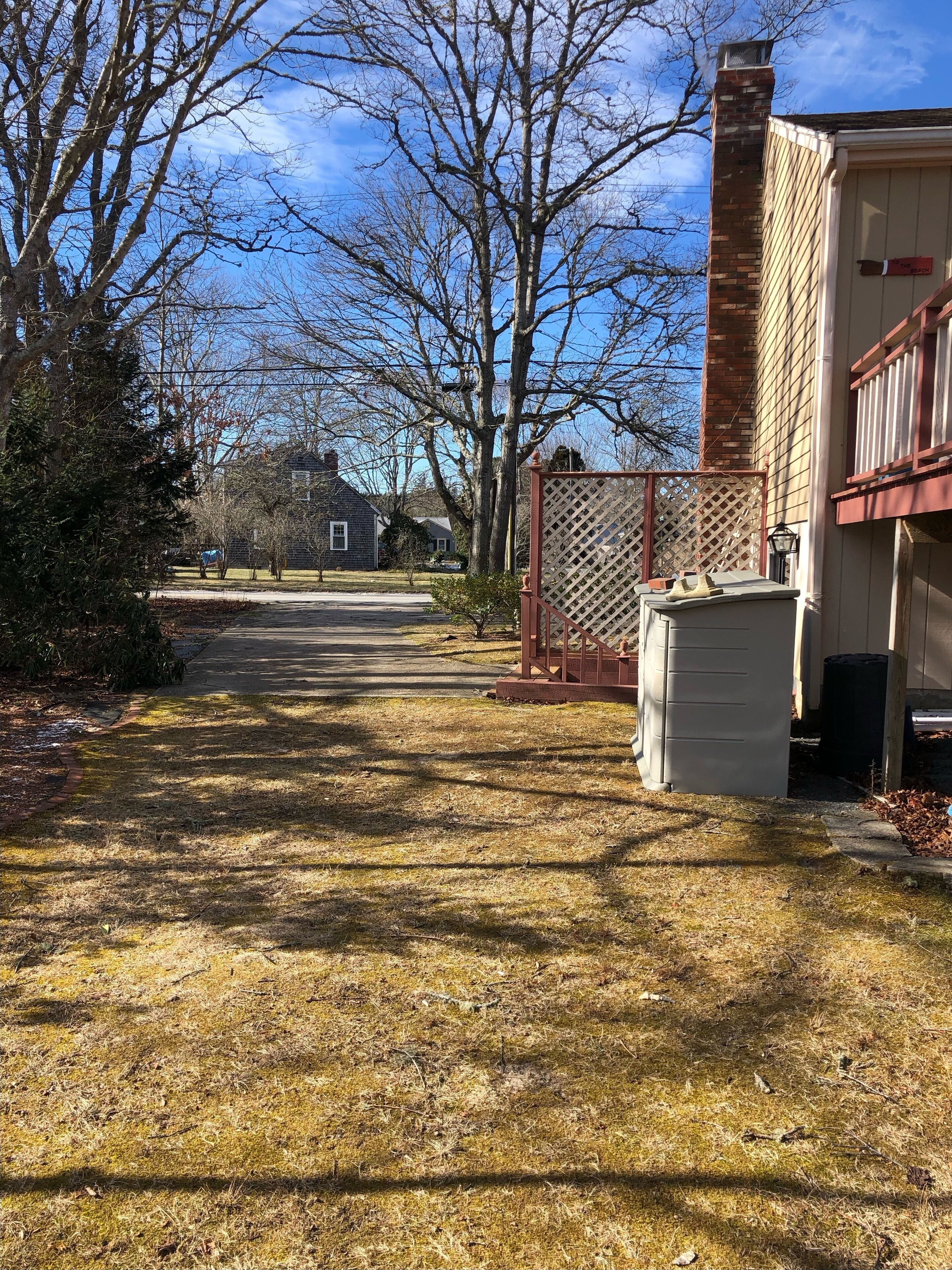 A residential area with a paved driveway leading to a house, a wooden fence, and a brick chimney.