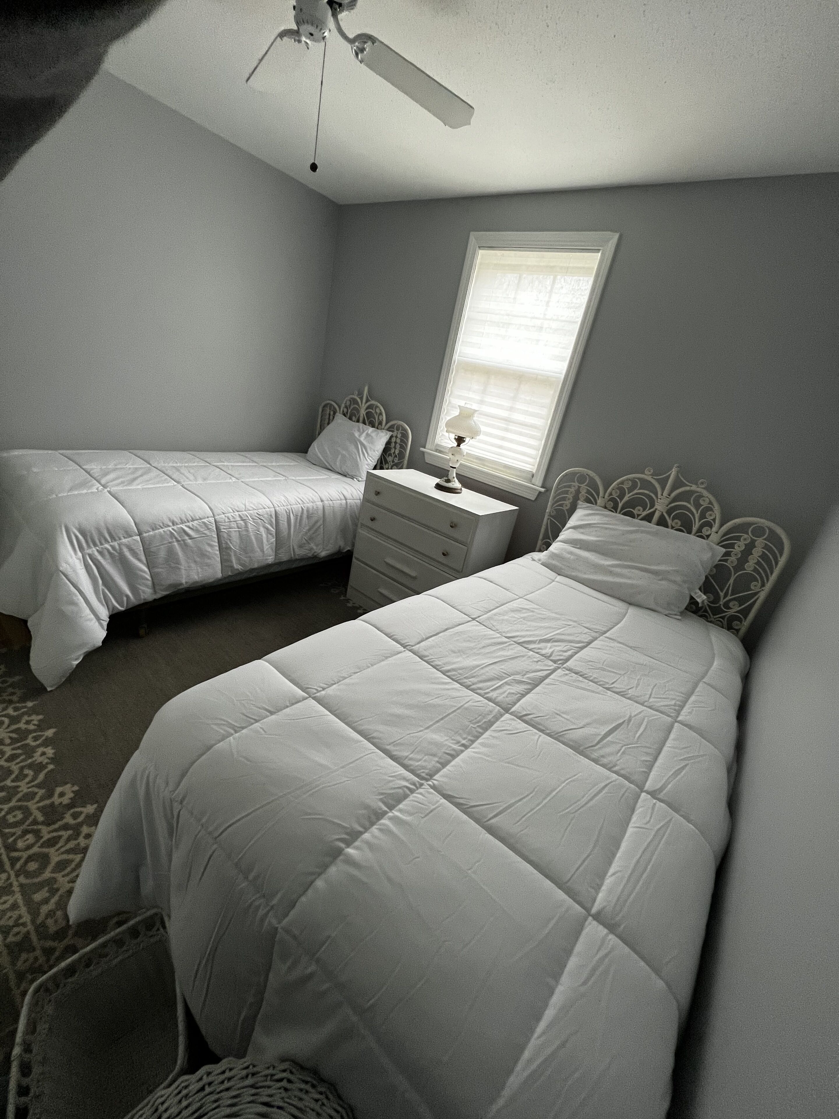 A bedroom with two single beds, a dresser, a ceiling fan, and a window.