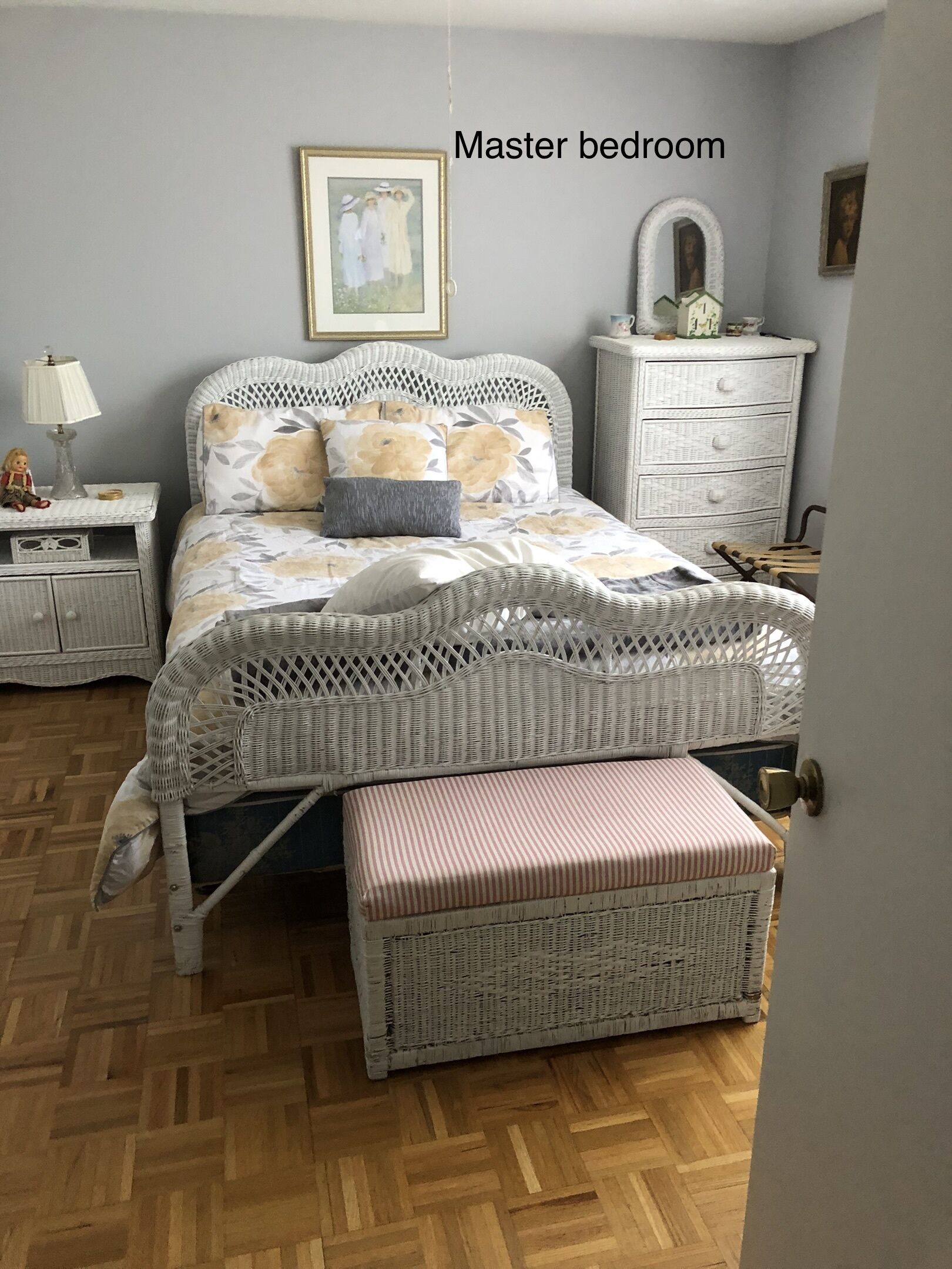Un dormitorio principal con una cama de mimbre, una mesita de noche con lámpara, un aparador y un banco.