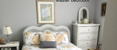 Un dormitorio principal con una cama de mimbre, una mesita de noche con lámpara, un aparador y un banco.