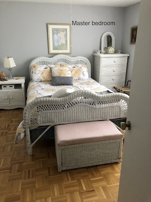 Ein Schlafzimmer mit einem Korbmöbelbett, einem Nachttisch mit Lampe, einer Kommode und einer Bank.