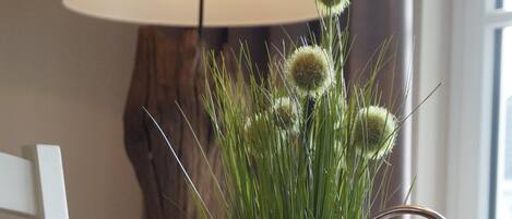 Een tafel met een kaars, een glazen pot met kralen en een potplant met groen gras en bolvormige uiteinden.