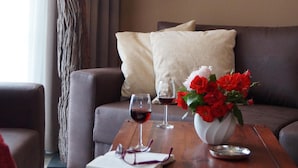 Uma sala de estar aconchegante com um sofá, uma mesa de centro com um vaso de flores vermelhas, uma taça de vinho e um abajur.