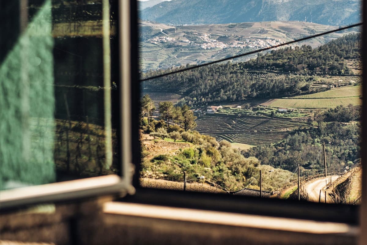 A window view of a rural landscape with fields, hills, and a distant town.