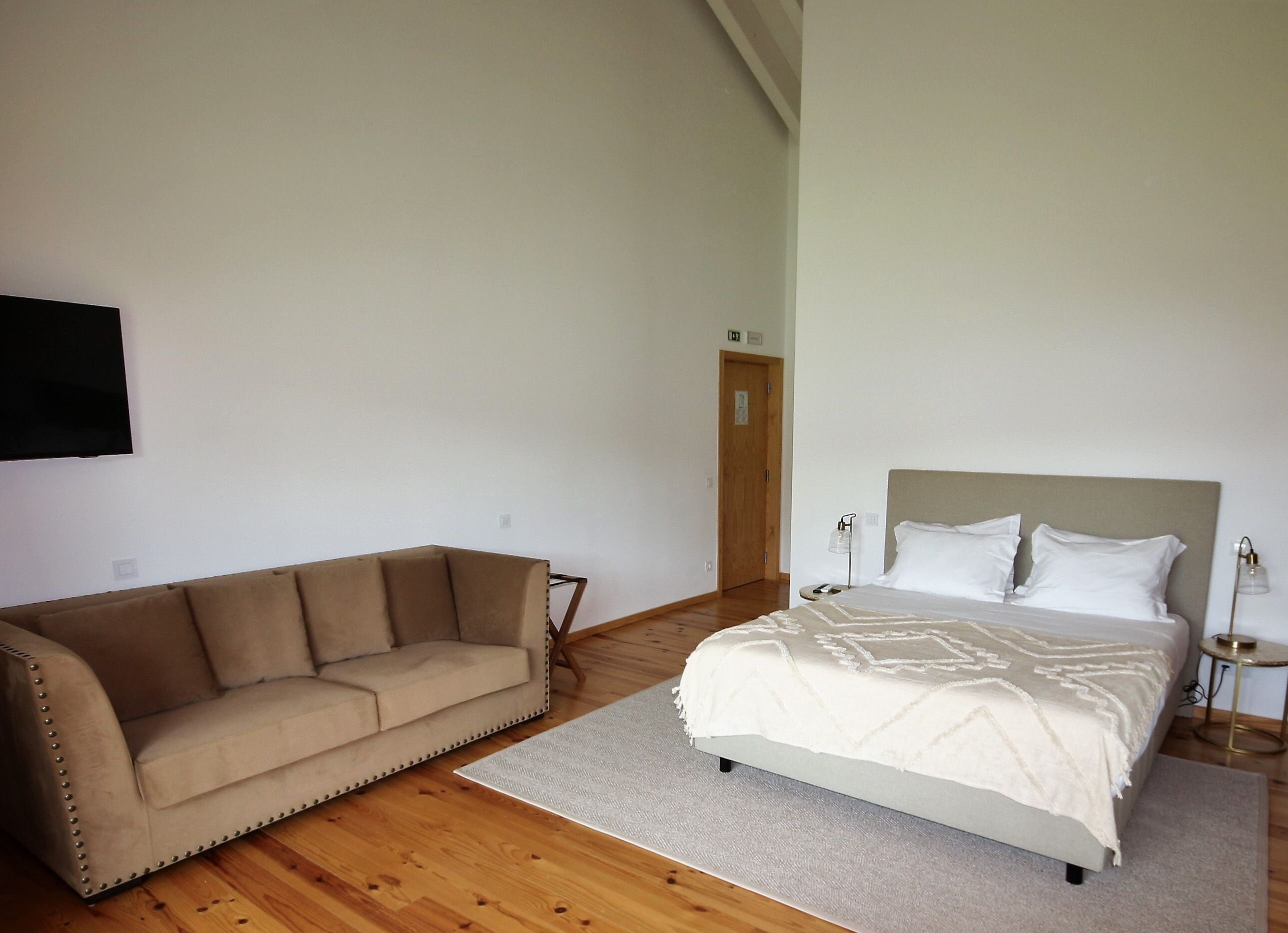 A bedroom with a bed, a sofa, and a TV mounted on the wall.