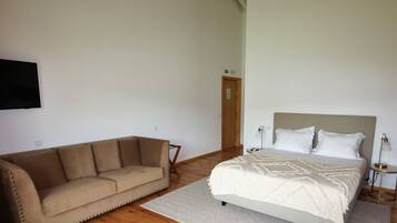 A bedroom with a bed, a sofa, and a TV mounted on the wall.
