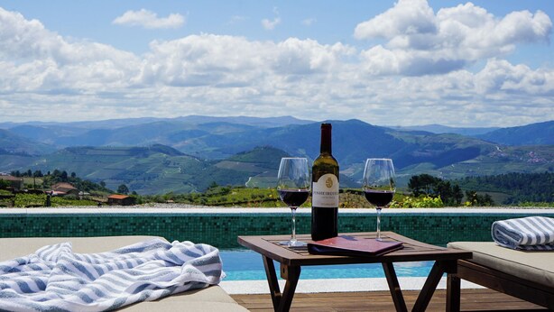 A poolside setting with a bottle of wine and glasses, a towel, and a view of distant mountains. - Casa do Santo - Wine & Tourism (Sabrosa)