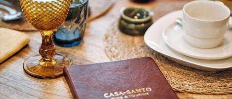 A table with a book titled 'CASA SANTO WINE & TOURISM', a glass with a textured pattern, and a white cup on a saucer.