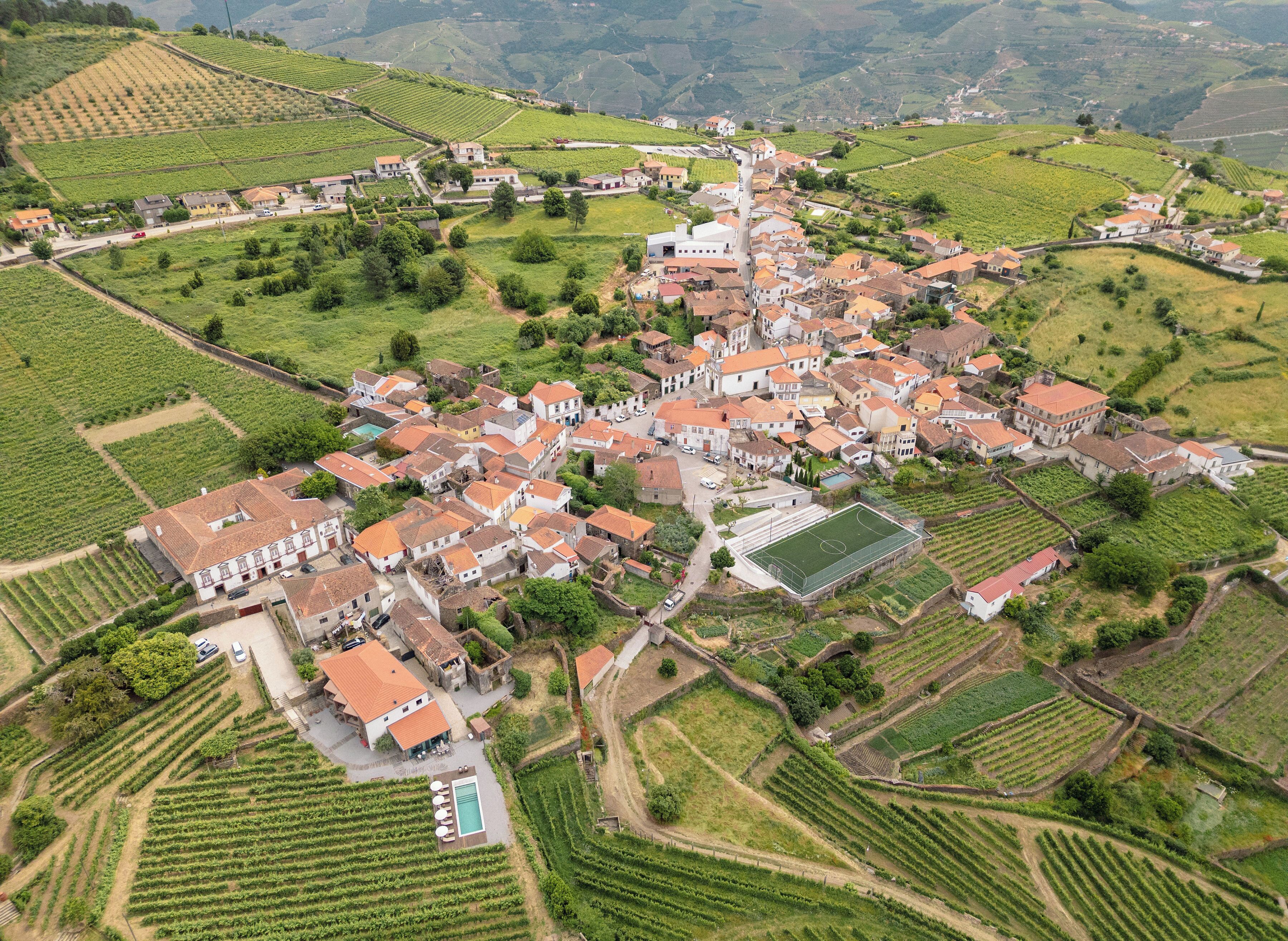 Vue aérienne d’un village avec des vignobles en terrasses, des bâtiments traditionnels et une place centrale.
