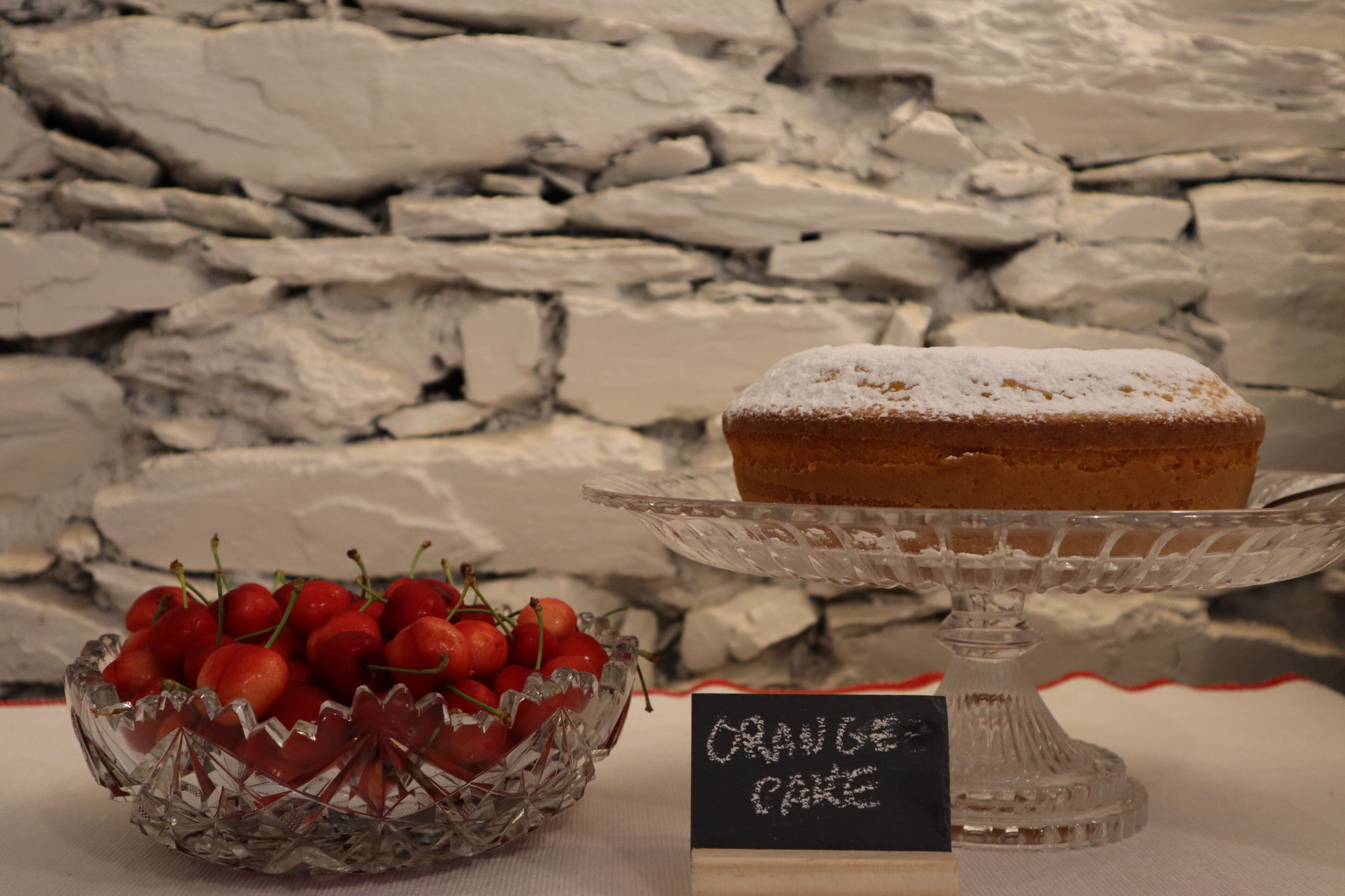 A dessert display with a cake on a stand and a bowl of cherries.