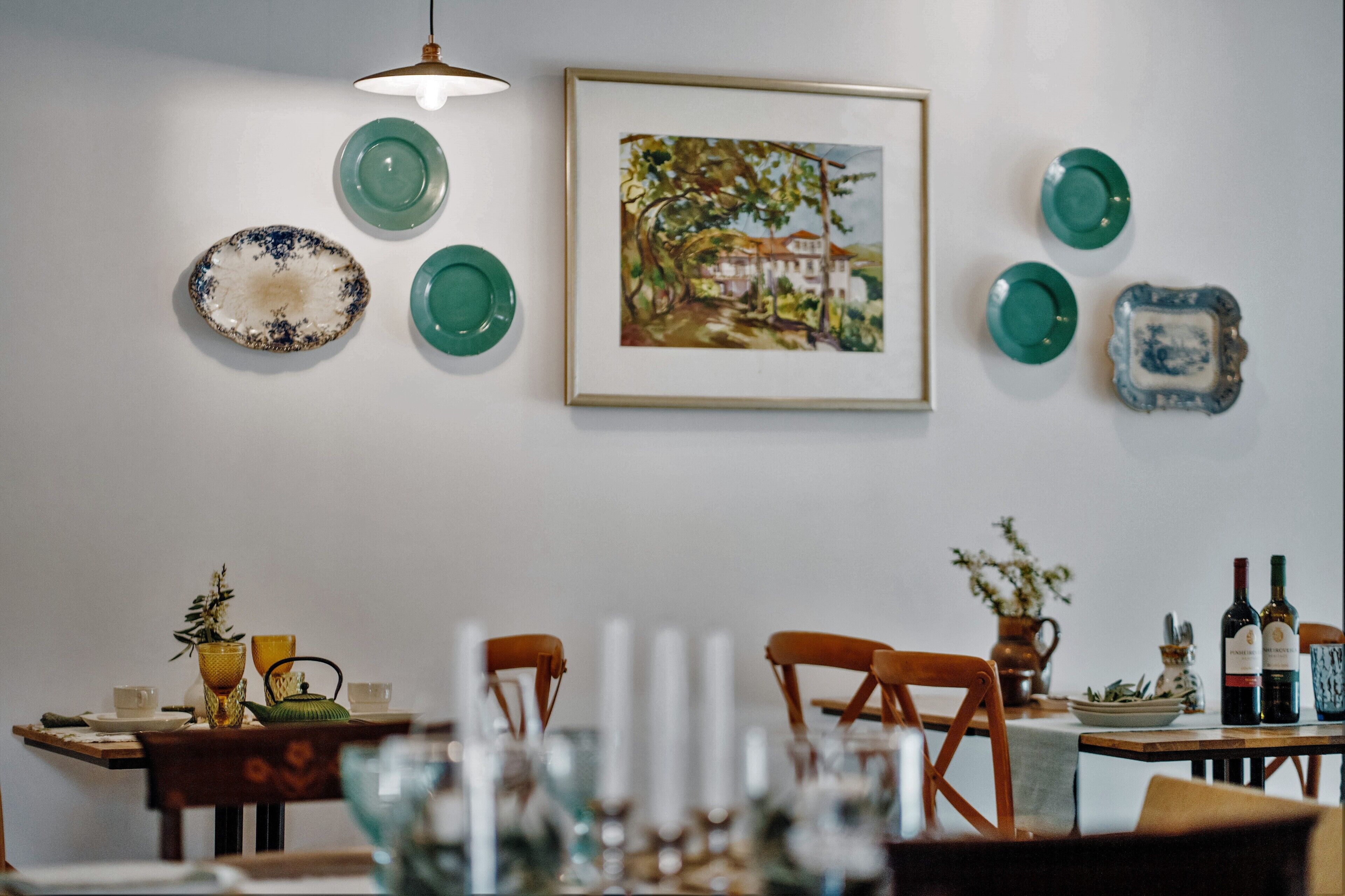 Un coin repas avec une table dressée pour deux personnes, un tableau encadré et diverses assiettes décoratives accrochées au mur.