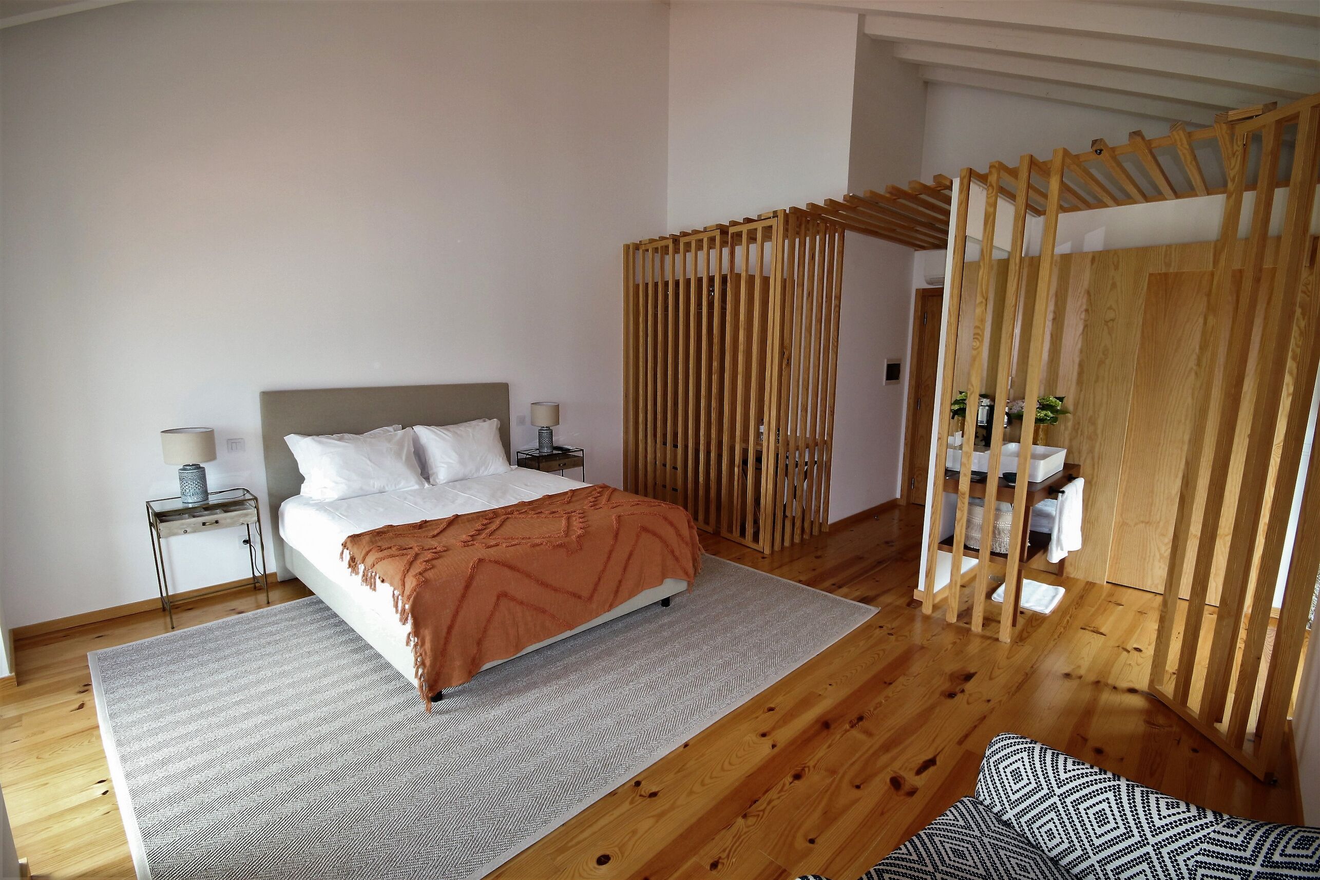 A bedroom with a bed, a nightstand, a wooden partition, and a small table with a lamp.