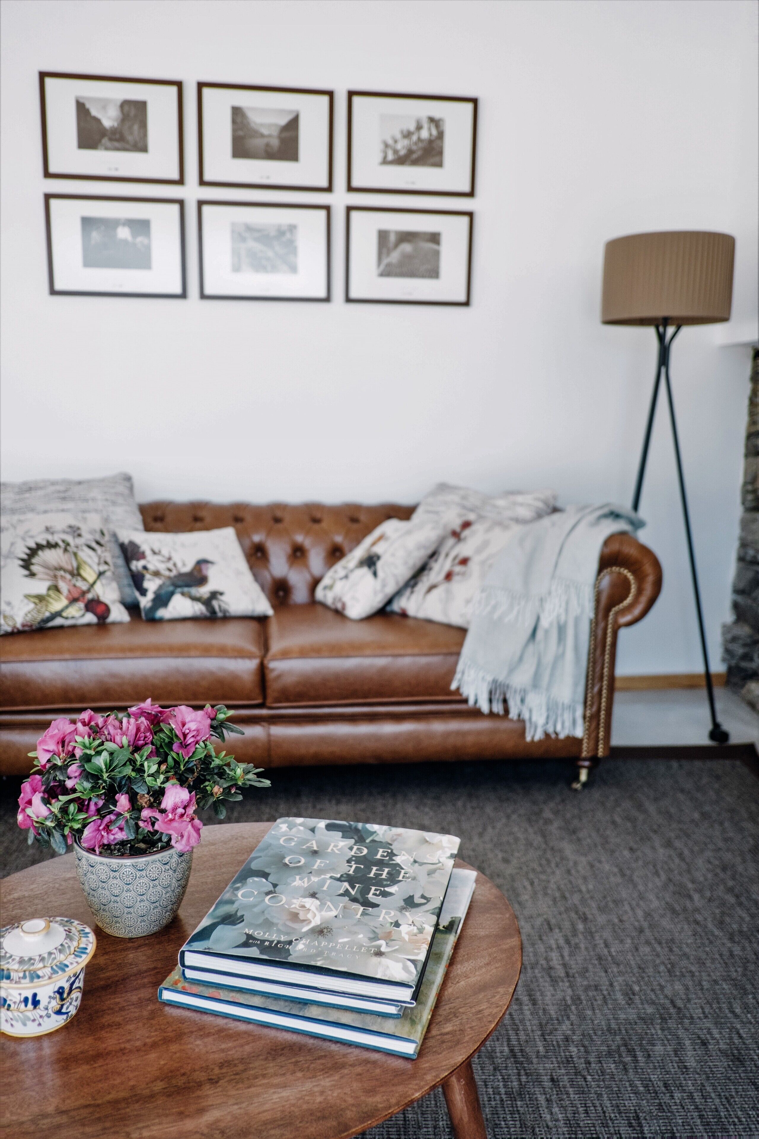 Un salon avec un canapé en cuir marron, une table basse ronde sur laquelle sont posés des livres et un pot de fleurs, et un lampadaire.