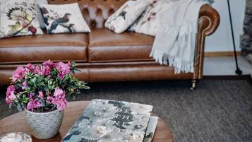 Un salon avec un canapé en cuir marron, une table basse ronde sur laquelle sont posés des livres et un pot de fleurs, et un lampadaire.