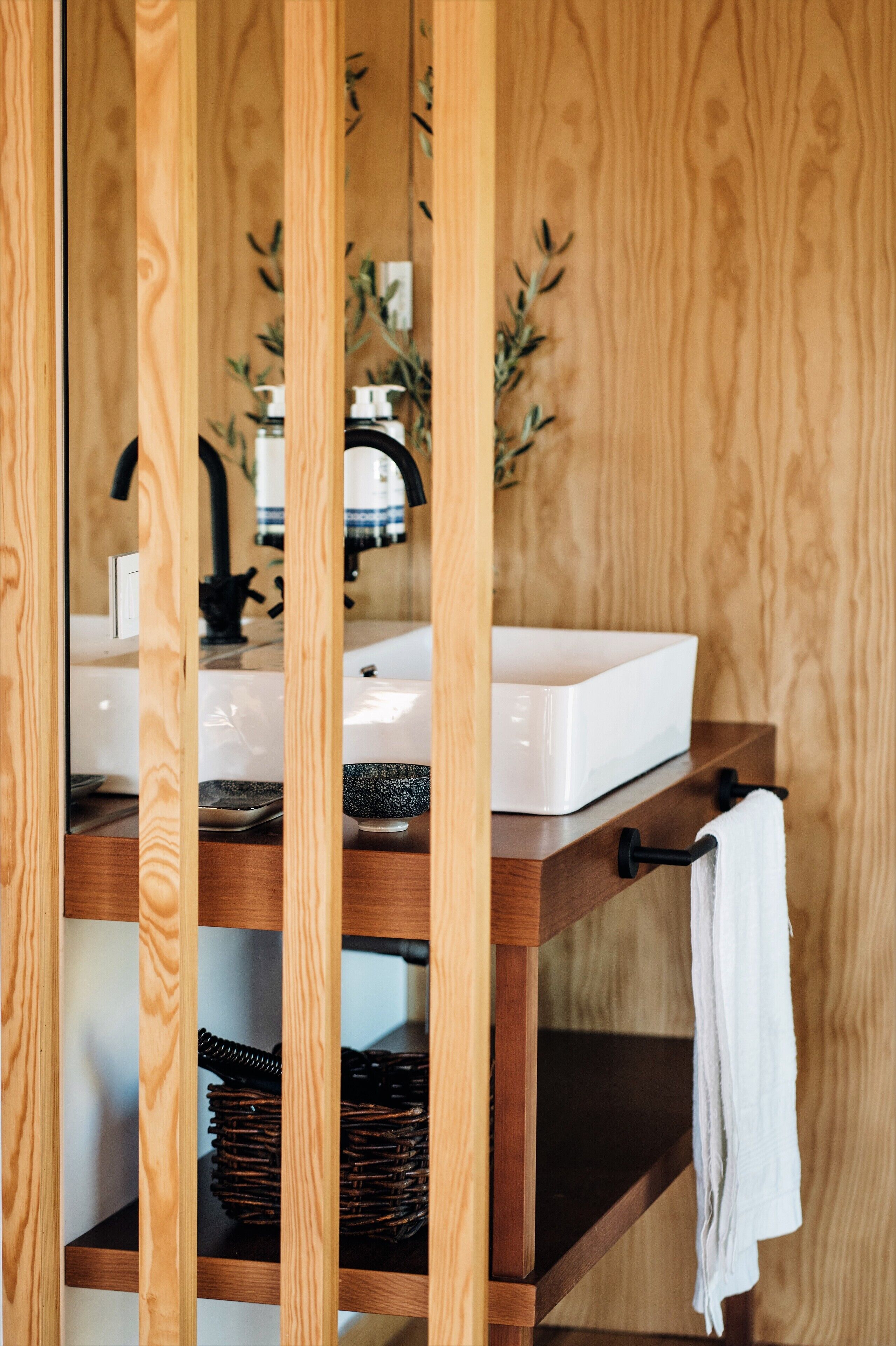 A wooden vanity with a white sink, a black faucet, and a towel hanging on a black hook.
