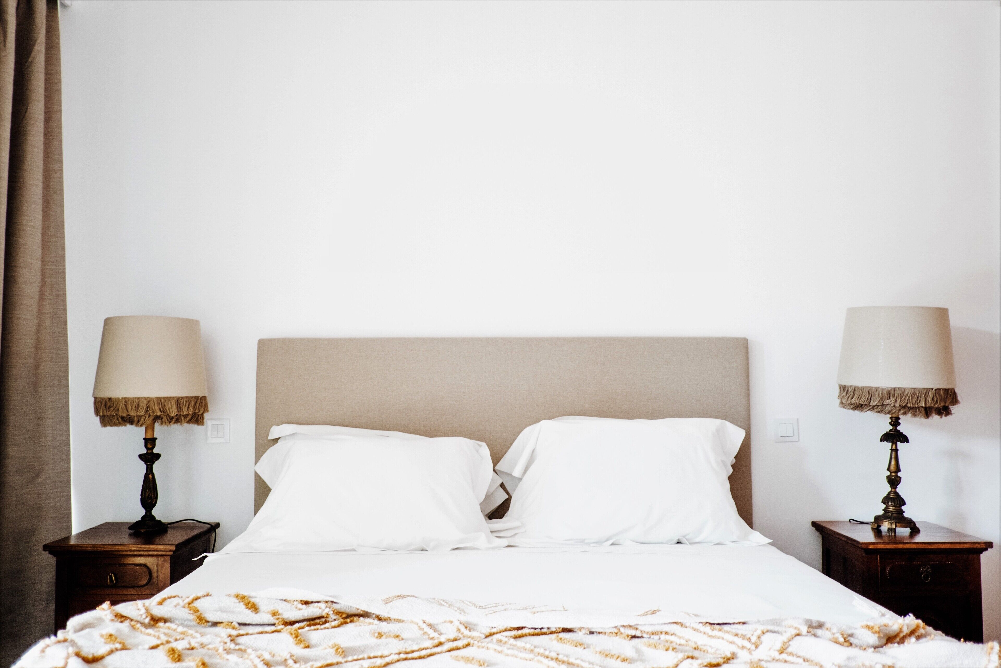 A neatly made bed with white linens and a patterned throw blanket, flanked by two bedside tables with lamps.