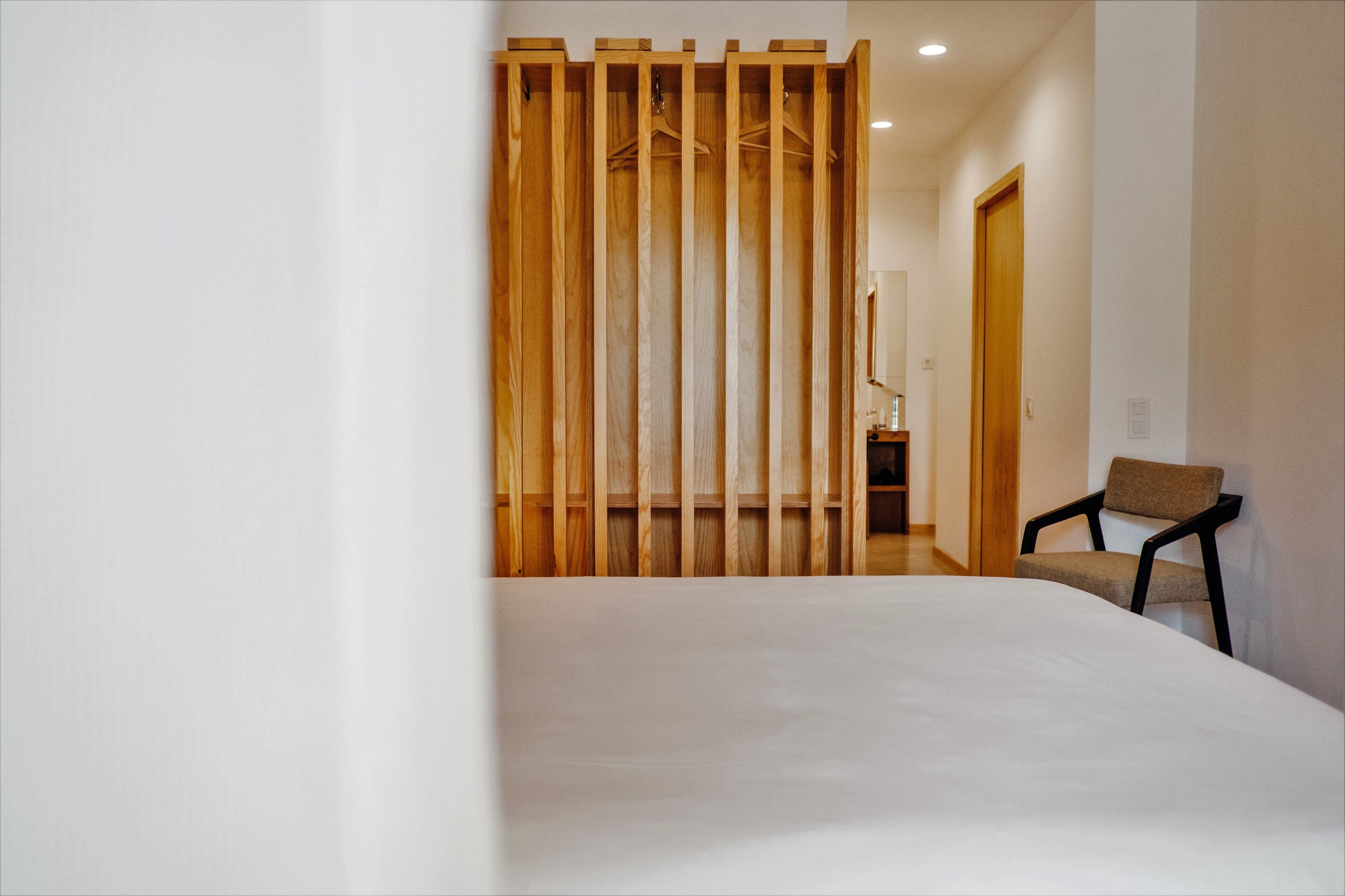 A bedroom with a bed, a wooden partition, a chair, and a door leading to another room.