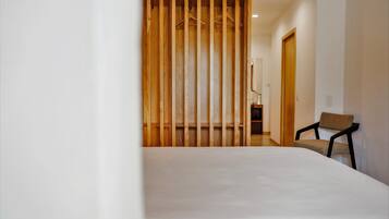 A bedroom with a bed, a wooden partition, a chair, and a door leading to another room.