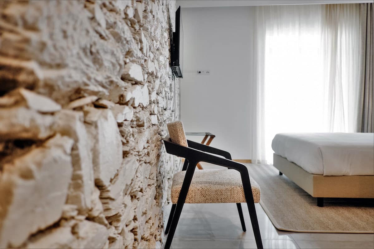 A modern bedroom with a stone wall, a bed, a chair, and a TV mounted on the wall.