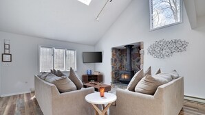 Een moderne woonkamer met een stenen open haard, twee banken, een televisie en een bijzettafeltje.
