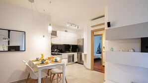 A modern kitchen with white cabinets, a dining area with a white table and chairs, and a small island with a sink. - Martilla - Two Bedroom Apartment, Sleeps 5 (Gabicce Mare)