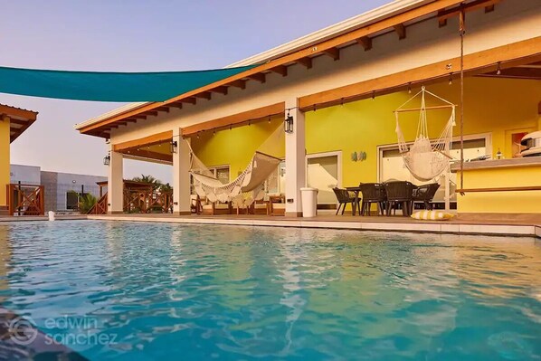 Une piscine dotée d’un espace détente couvert, comprenant des chaises et un hamac.