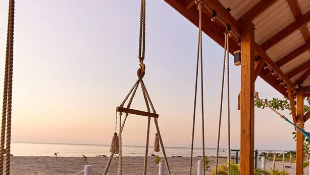 A wooden deck with a swing chair overlooking a beach. - Spectacular oceanfront home (Omoa)