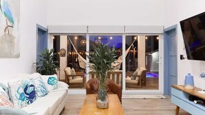 A modern living room with a sofa, coffee table, and a TV. There is a sliding glass door leading to a balcony with chairs and a table. - Spectacular oceanfront home (Omoa)