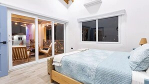 A bedroom with a bed, a window, and a sliding glass door leading to a balcony with chairs. - Spectacular oceanfront home (Omoa)