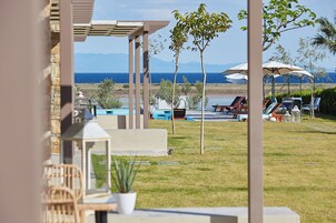 Un área junto a la piscina con sillones de descanso, sombrillas y vista al mar.