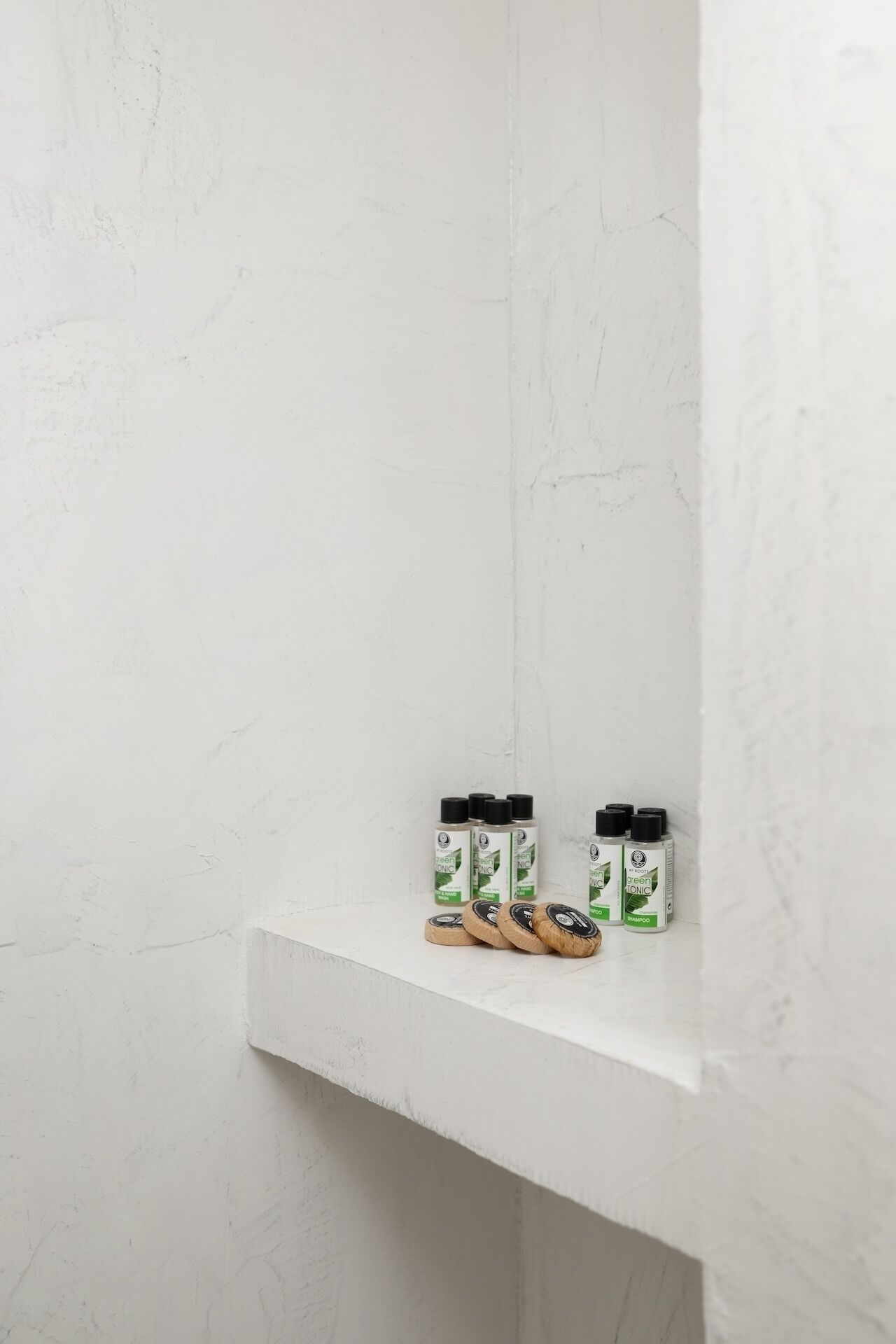 Un estante blanco con dos botellas de champú tónico verde y un par de zapatillas marrones.