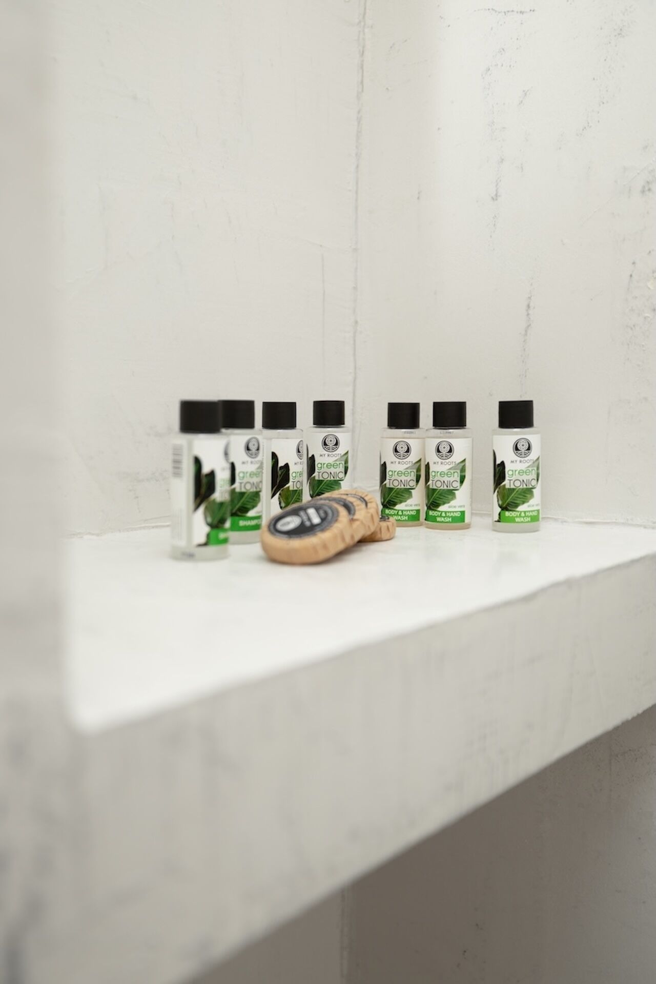 Una estantería blanca con cuatro botellas de gel de ducha tónico verde y un cepillo de madera.