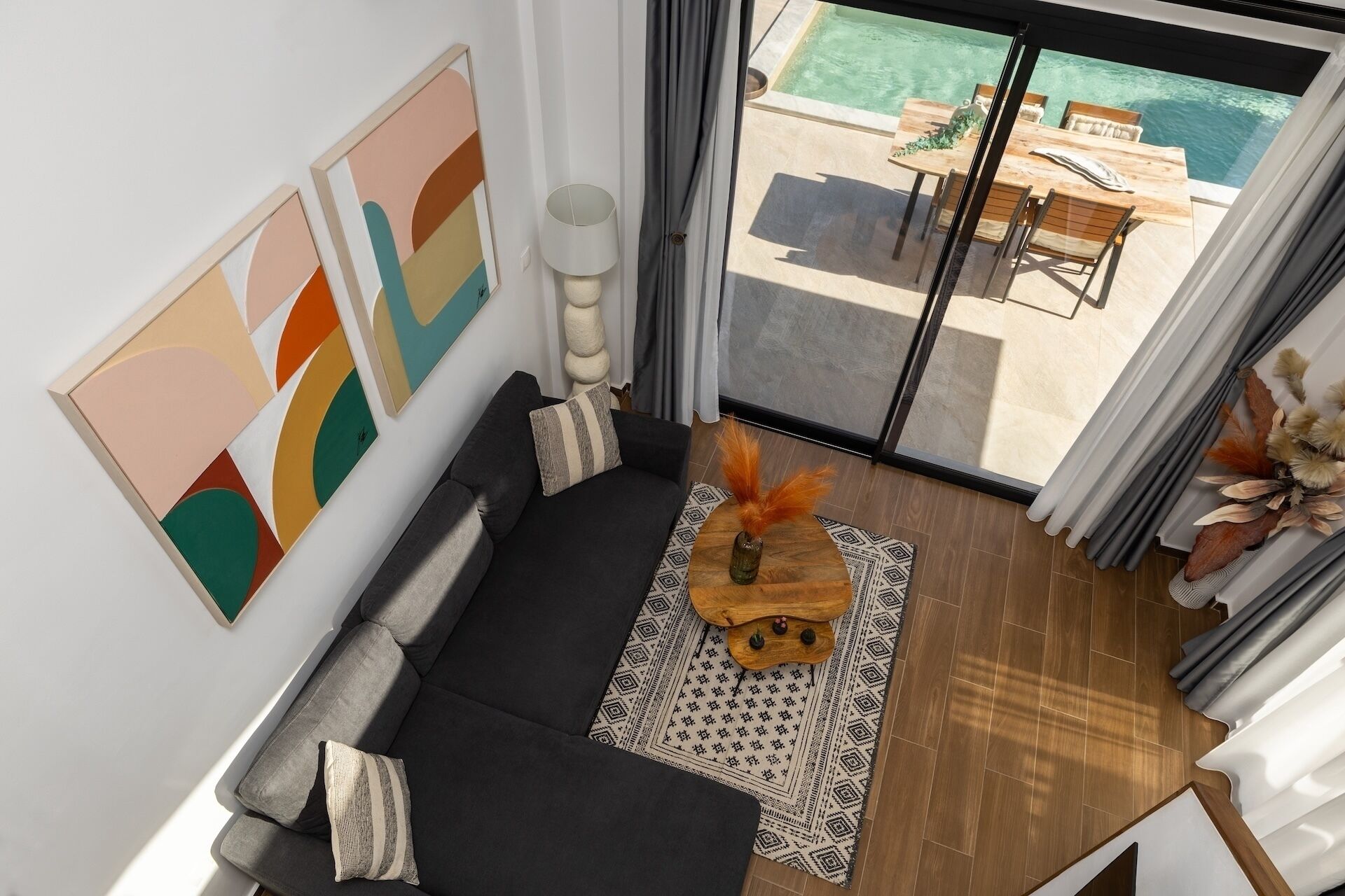 A modern living room with a black sofa, a wooden coffee table with decorative items, and a view of an outdoor pool area through a glass door.