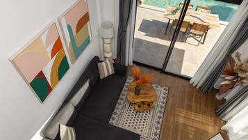 A modern living room with a black sofa, a wooden coffee table with decorative items, and a view of an outdoor pool area through a glass door.