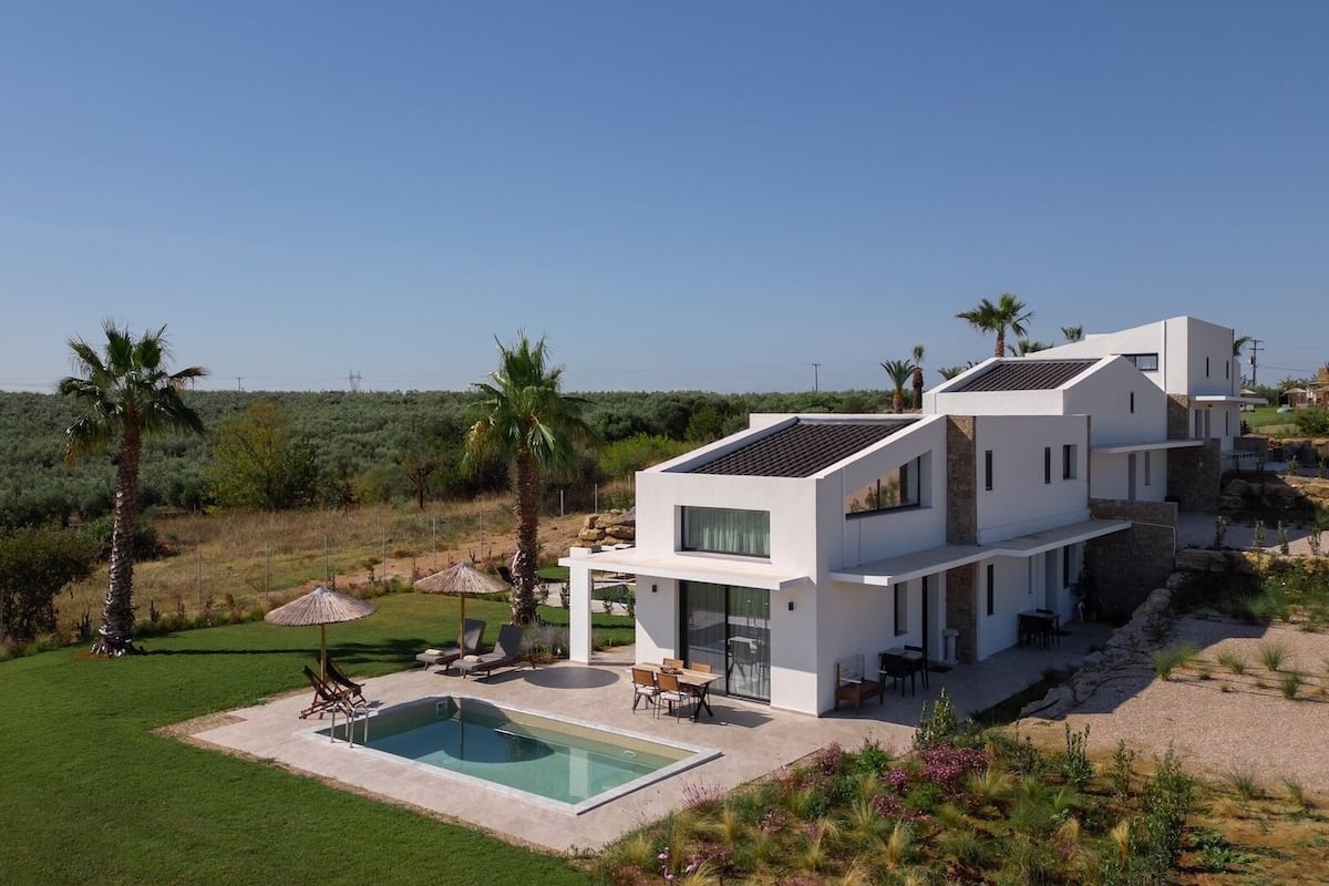Una casa moderna de dos pisos amb una piscina, envoltada per un jardí ben cuidat i palmeres.