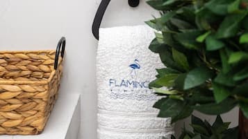 A bathroom with a white towel hanging on a black towel rack, a woven basket, and a plant.