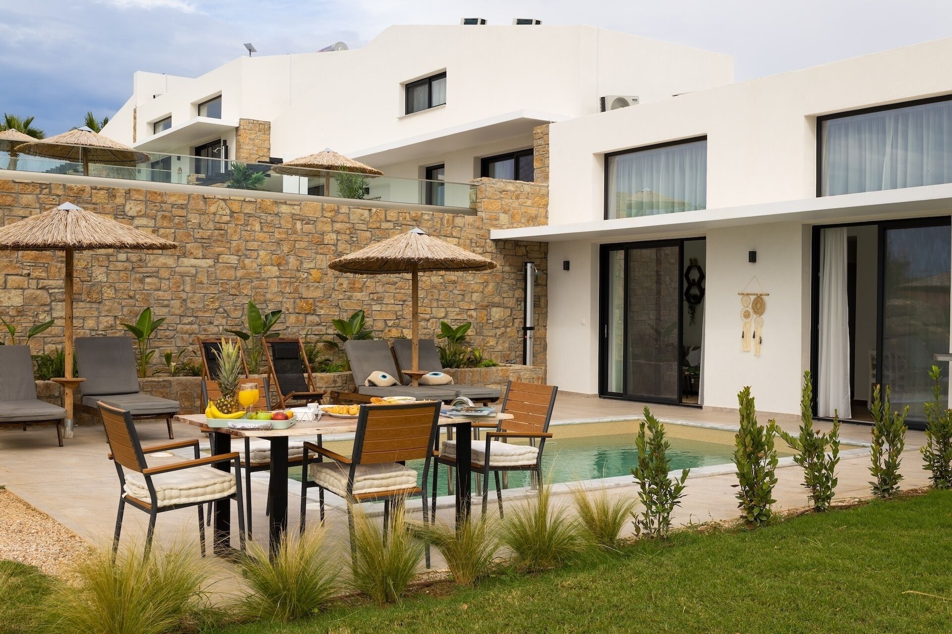A modern outdoor dining area with stone walls, umbrellas, and a pool.