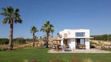 A modern two-story house with a patio area, surrounded by palm trees and a well-maintained lawn.