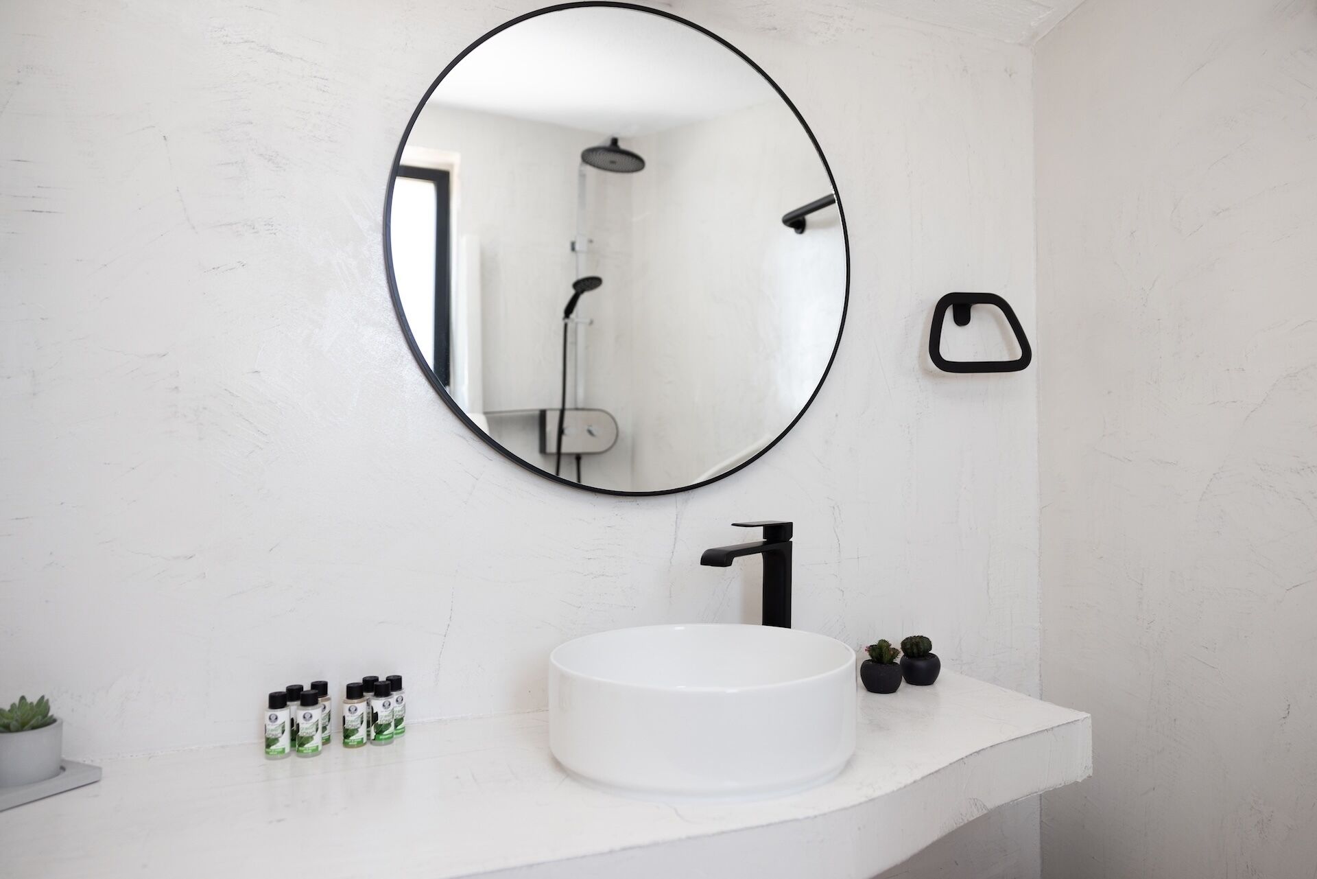 A bathroom with a round mirror, a white sink, and a shower visible in the background.