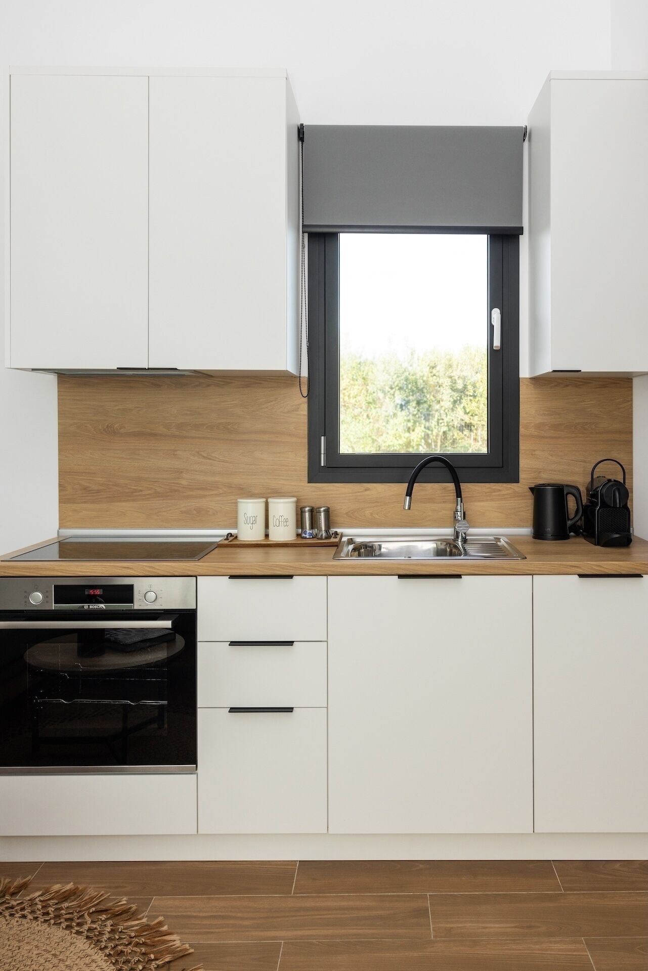 Cocina moderna con armarios blancos, un grifo negro, un horno Bosch y una ventana con vistas a zonas verdes.