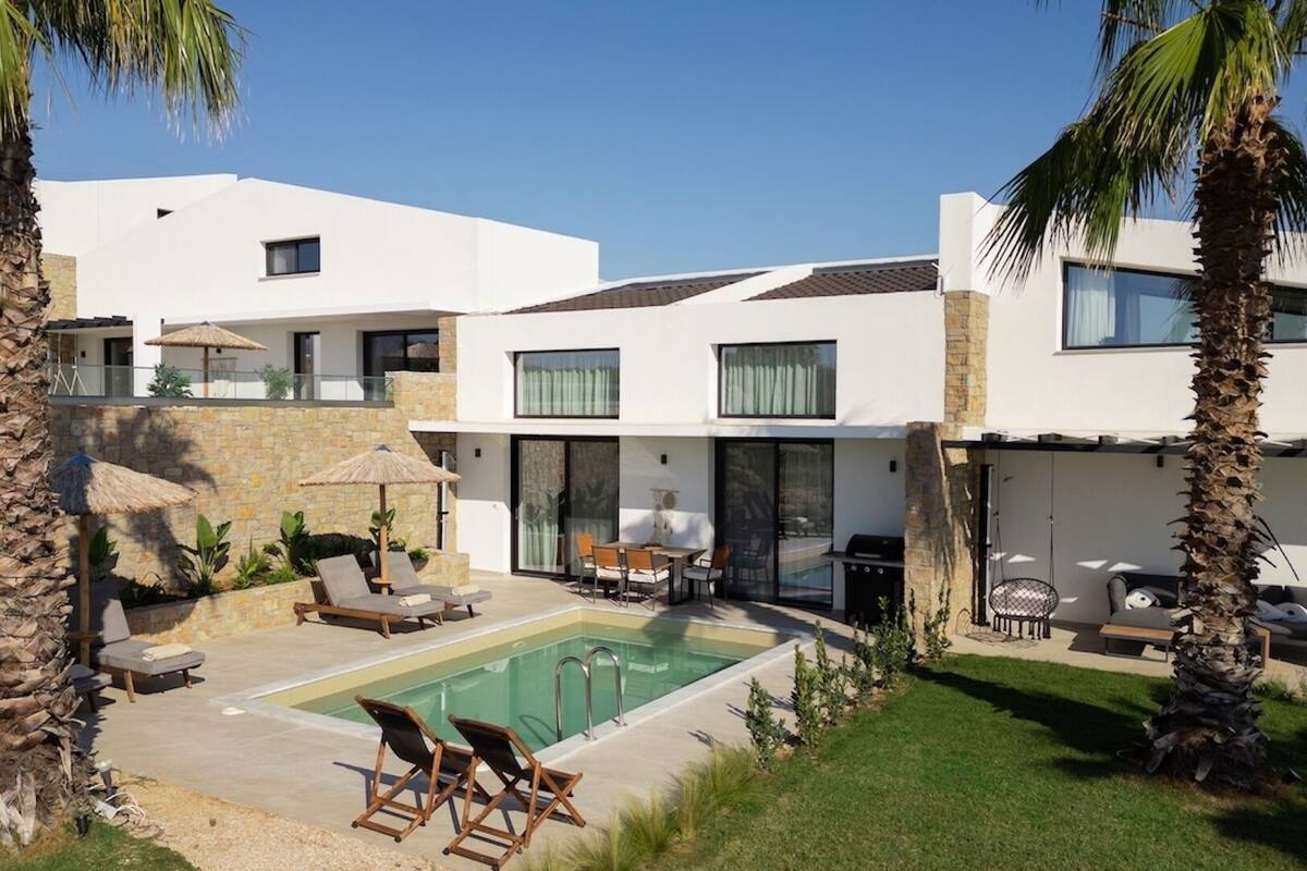 Una vila moderna amb piscina, mobiliari exterior i palmeres.