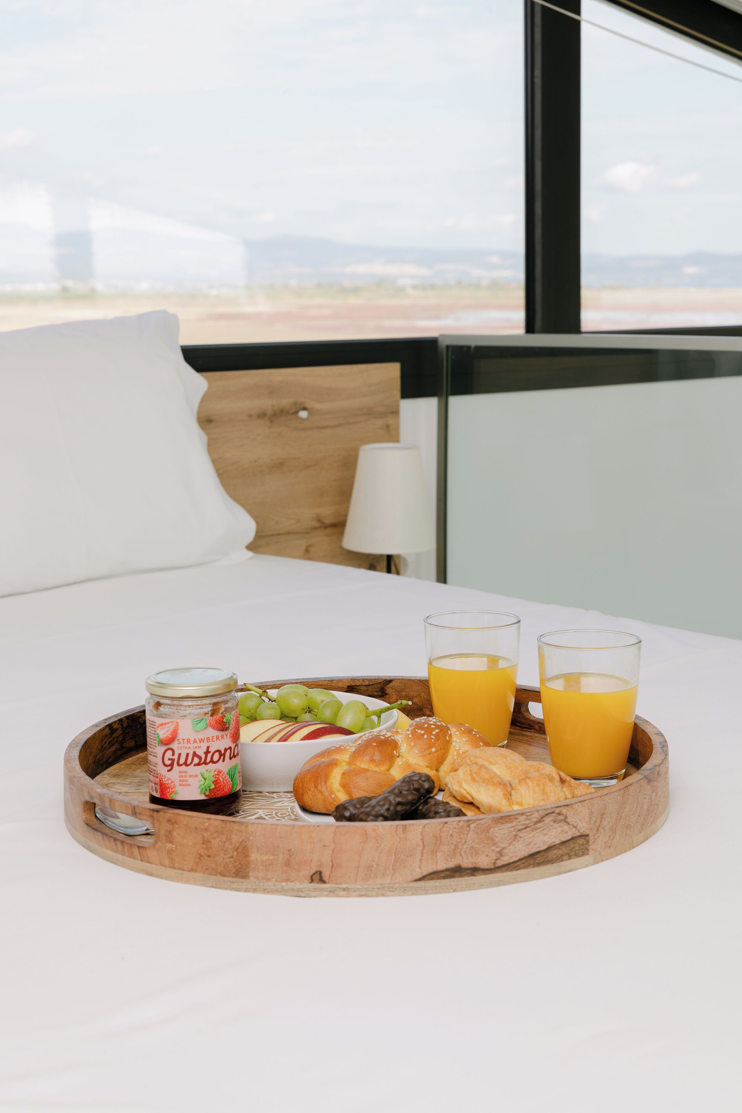 Een ontbijtkar met een pot aardbeienjam, druiven, croissants en sinaasappelsap op een bed met uitzicht op het strand.